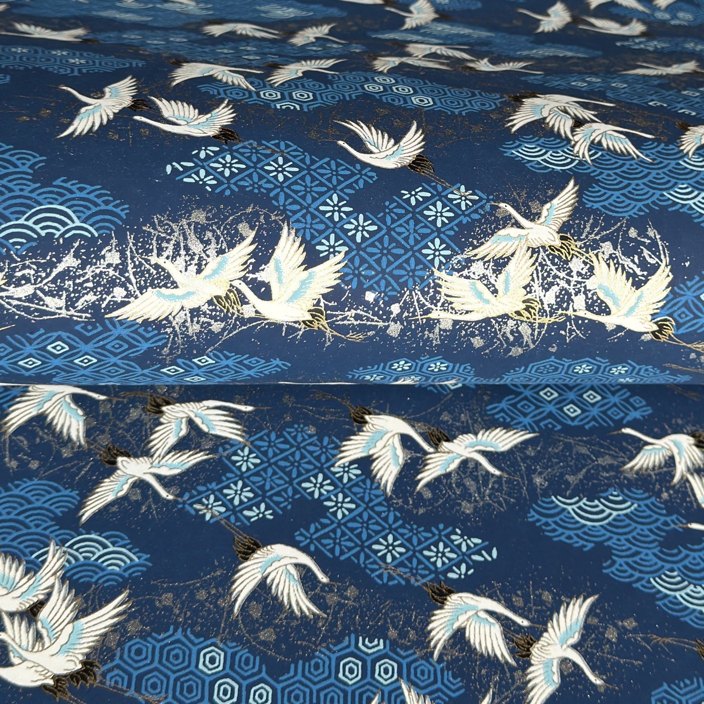 a sheet of Japanese chiyogami yuzen paper with a traditional pattern of white cranes flying with a deep blue background of patterned clouds