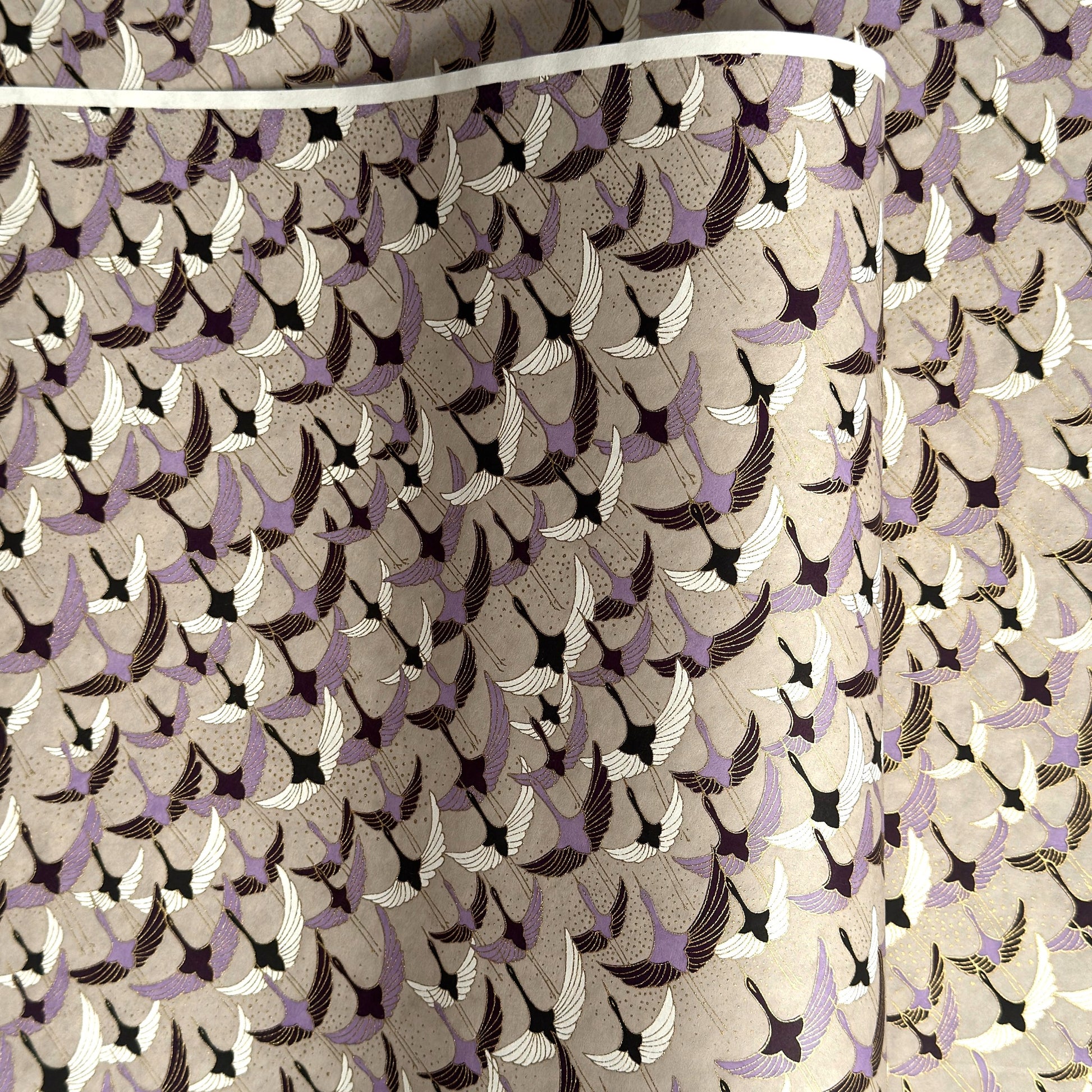 a sheet of Japanese chiyogami yuzen paper with a pattern of cranes in flight in lilac, black, taupe and gold
