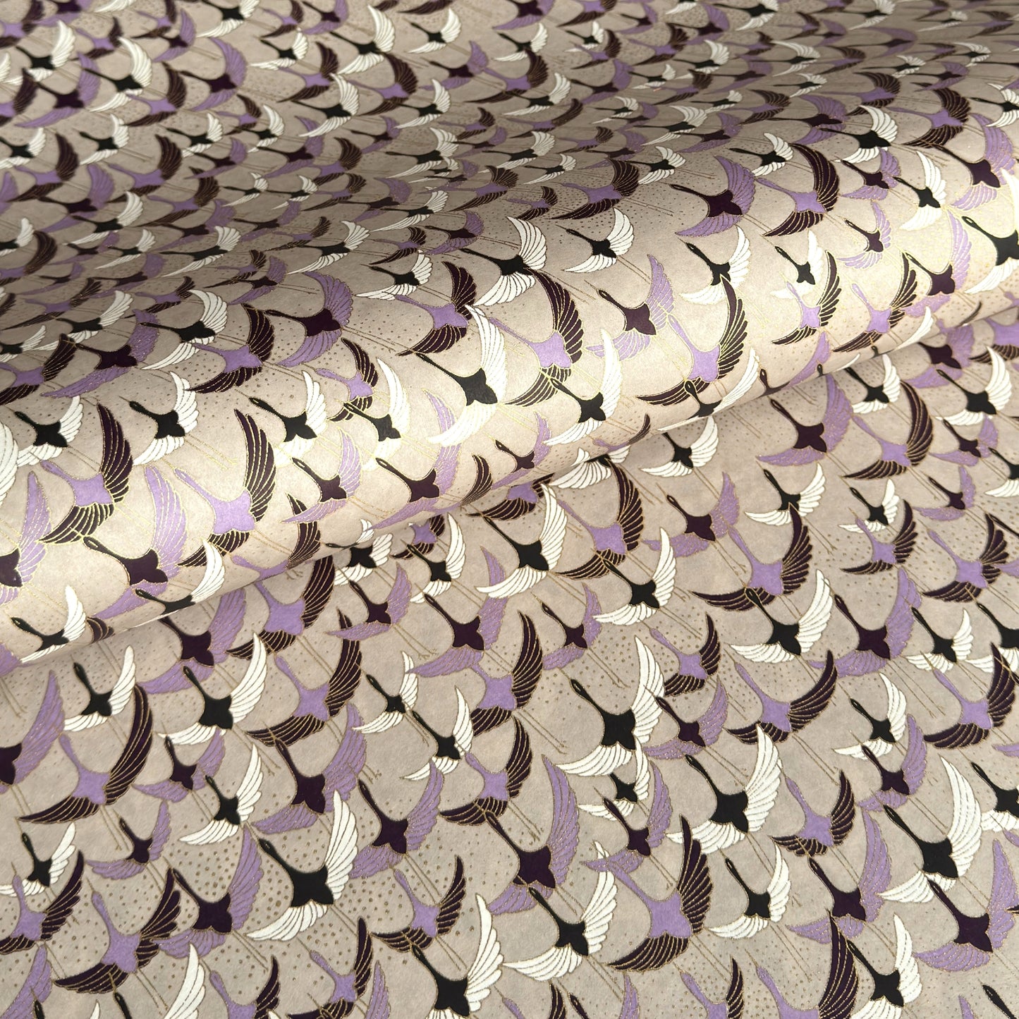 a sheet of Japanese chiyogami yuzen paper with a pattern of cranes in flight in lilac, black, taupe and gold