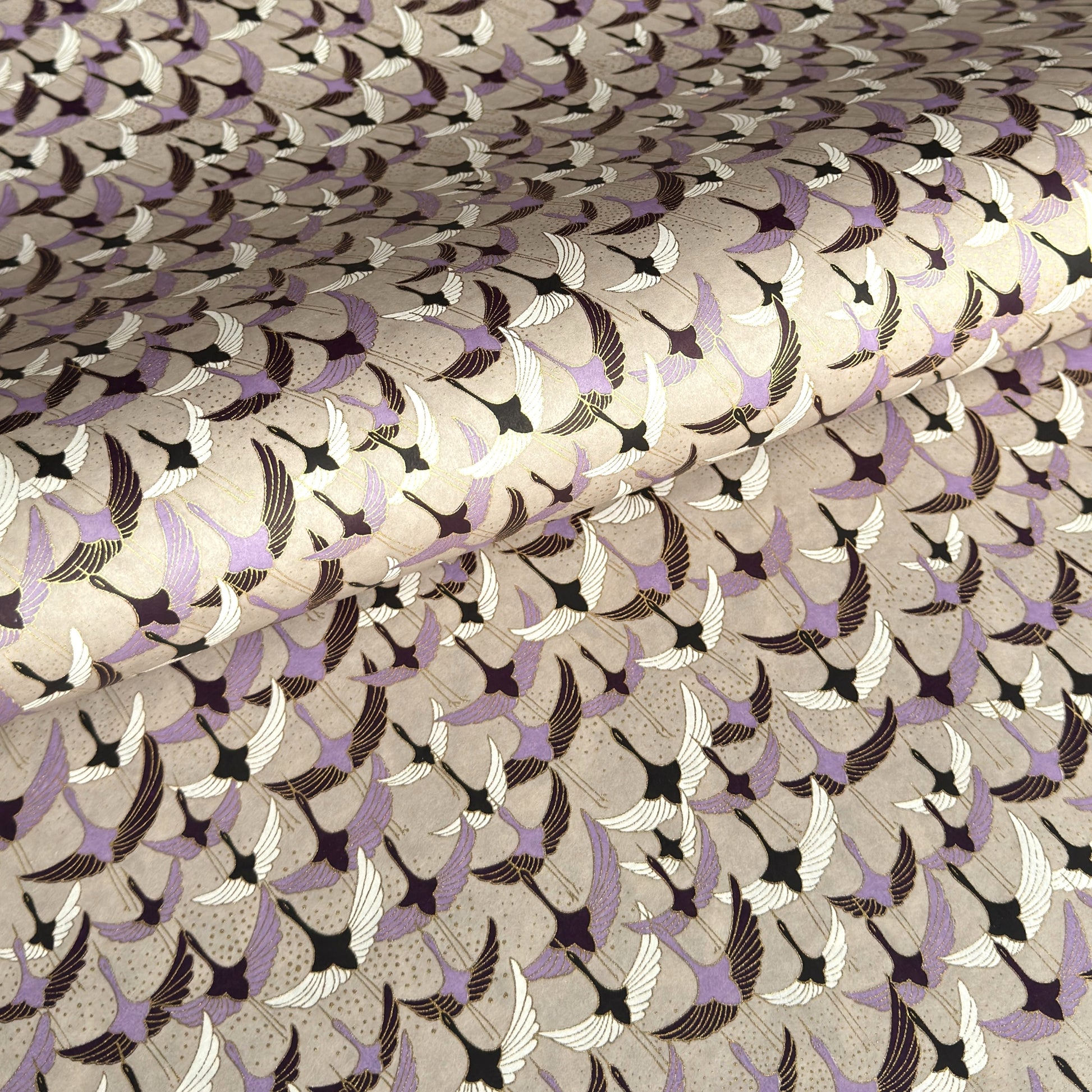 a sheet of Japanese chiyogami yuzen paper with a pattern of cranes in flight in lilac, black, taupe and gold