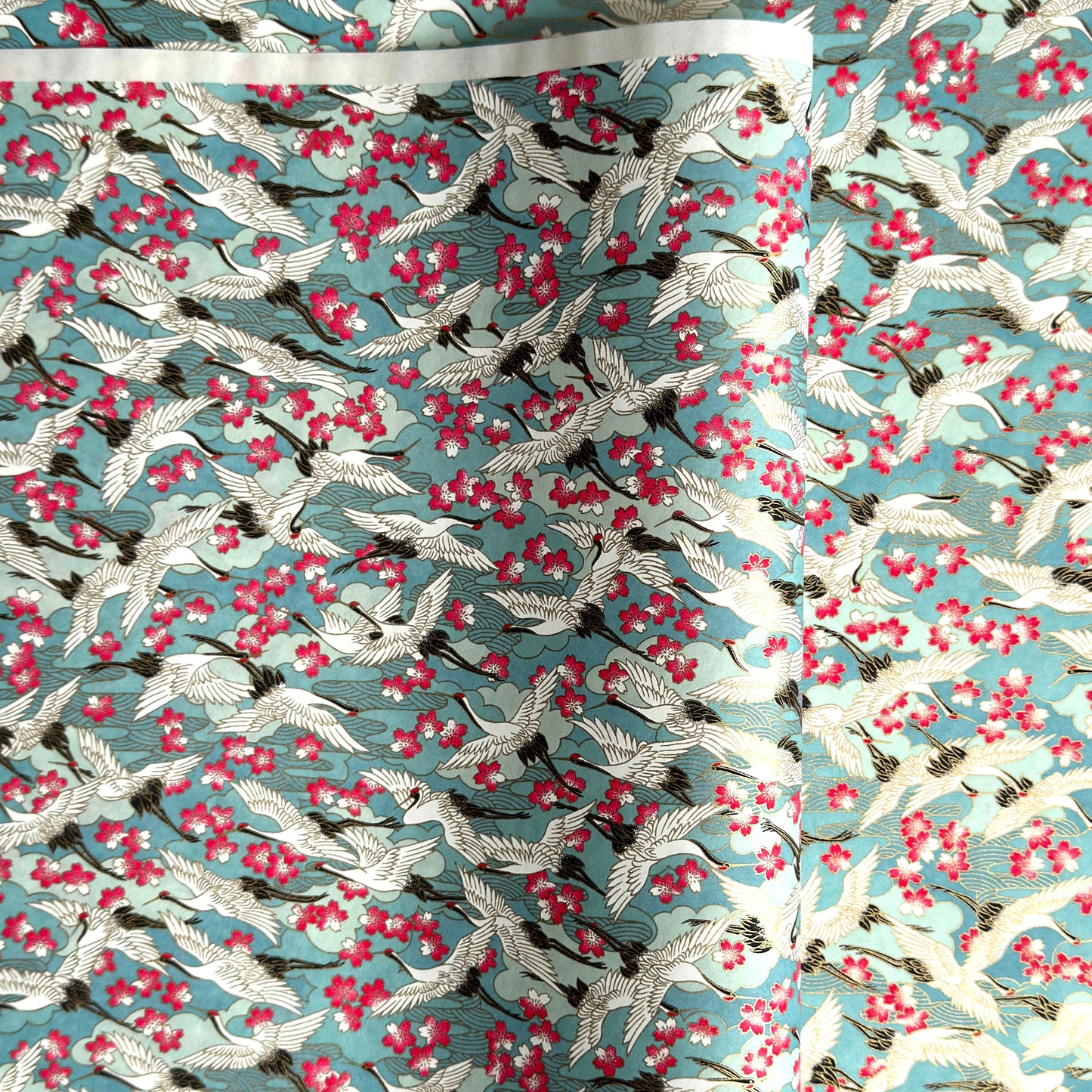 Japanese chiyogami paper with a pattern of white cranes, pink cherry blossom on a blue background. 