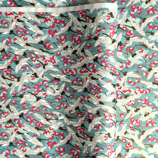 Japanese chiyogami paper with a pattern of white cranes, pink cherry blossom on a blue background. 