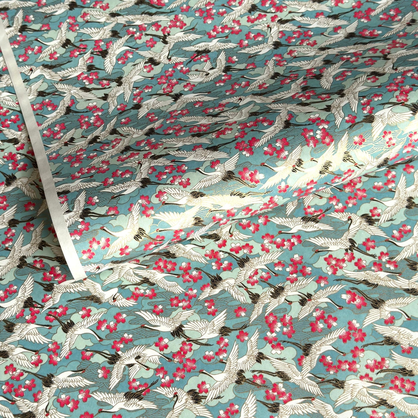 Japanese chiyogami paper with a pattern of white cranes, pink cherry blossom on a blue background. 