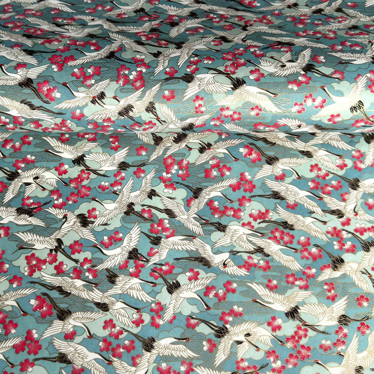 Japanese chiyogami paper with a pattern of white cranes, pink cherry blossom on a blue background. 