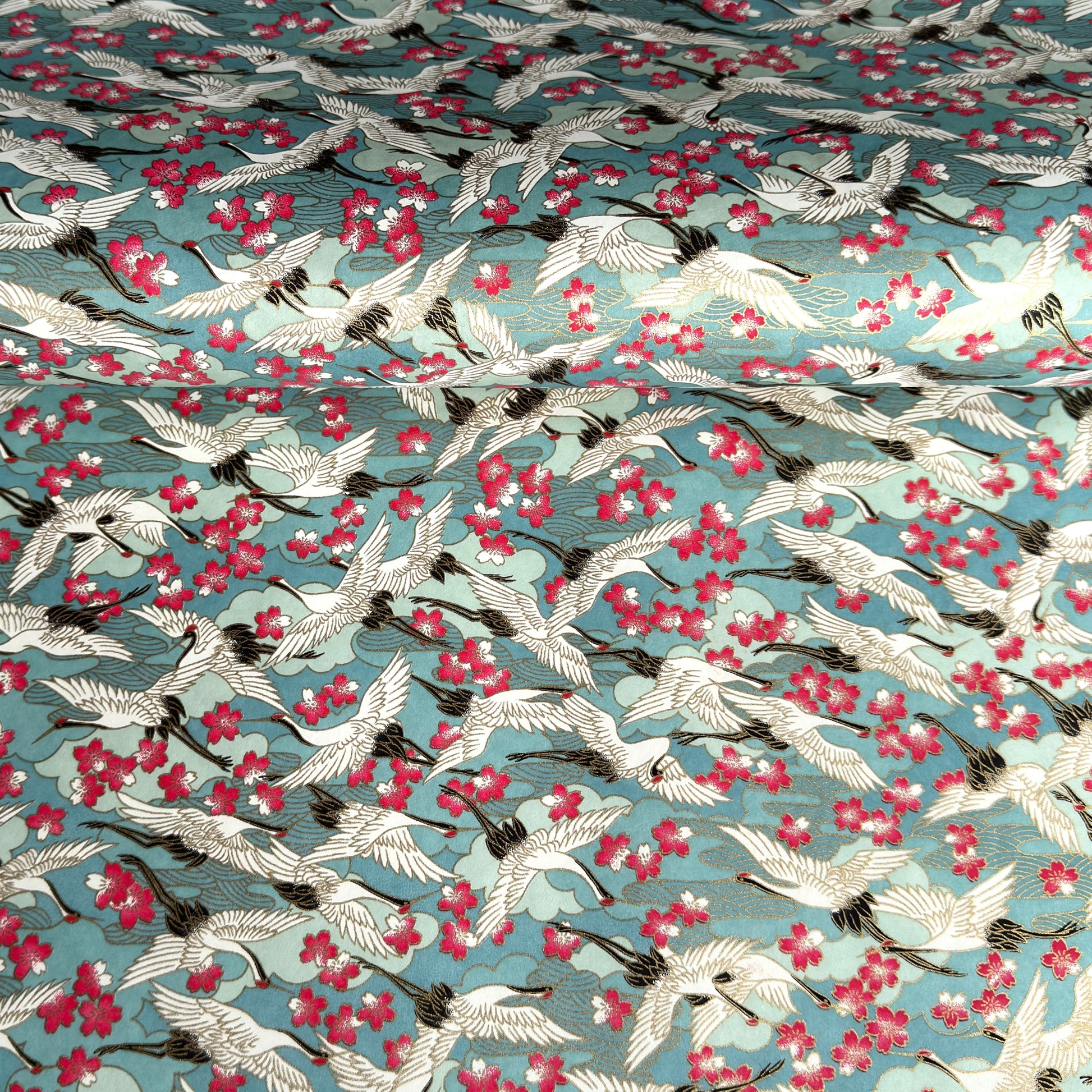 Japanese chiyogami paper with a pattern of white cranes, pink cherry blossom on a blue background. 