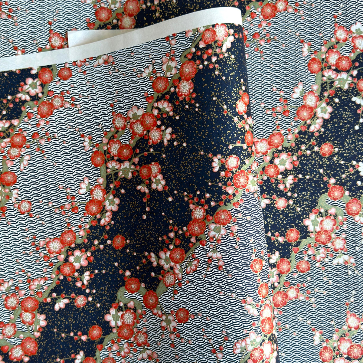 Diagonal branches of rich pink plum (ume) blossom on a midnight blue background with gold accents. Japanese chiyogami paper