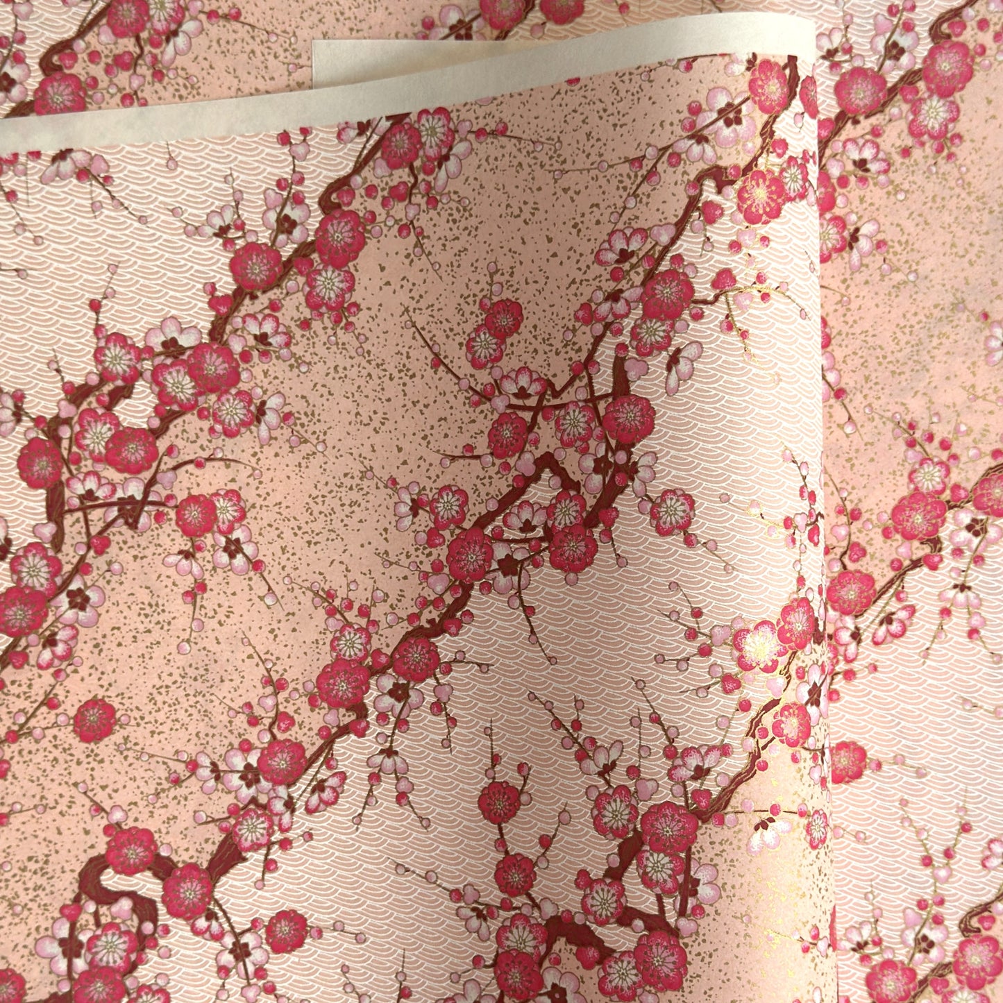 Diagonal branches of pink plum (ume) blossom on a light pink background with gold accents. Japanese chiyogami paper