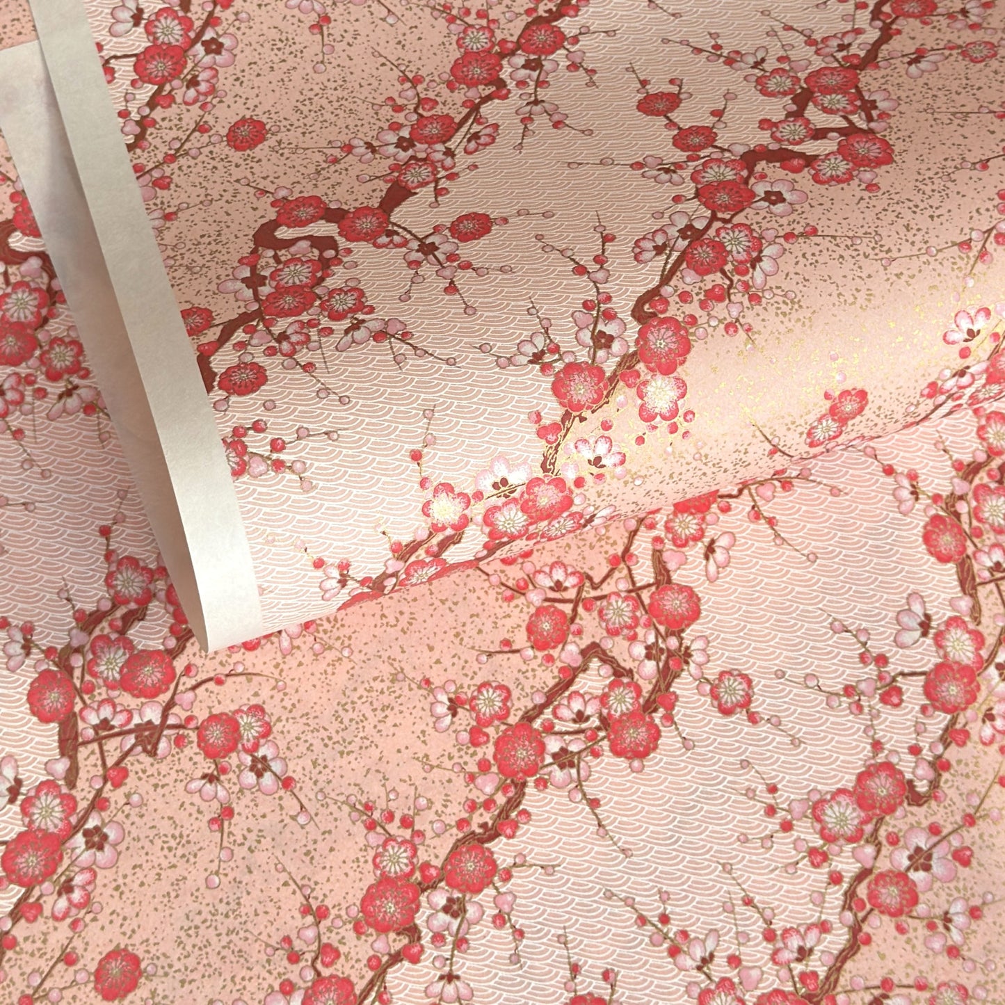 Diagonal branches of pink plum (ume) blossom on a light pink background with gold accents. Japanese chiyogami paper