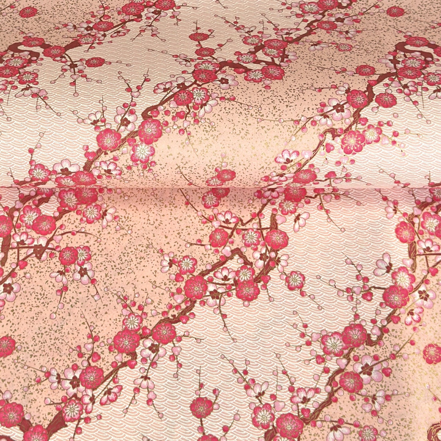 Diagonal branches of pink plum (ume) blossom on a light pink background with gold accents. Japanese chiyogami paper