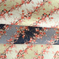 Japanese chiyogami silkscreen paper with diagonal branches of pink plum blossom on a sage green backdrop.