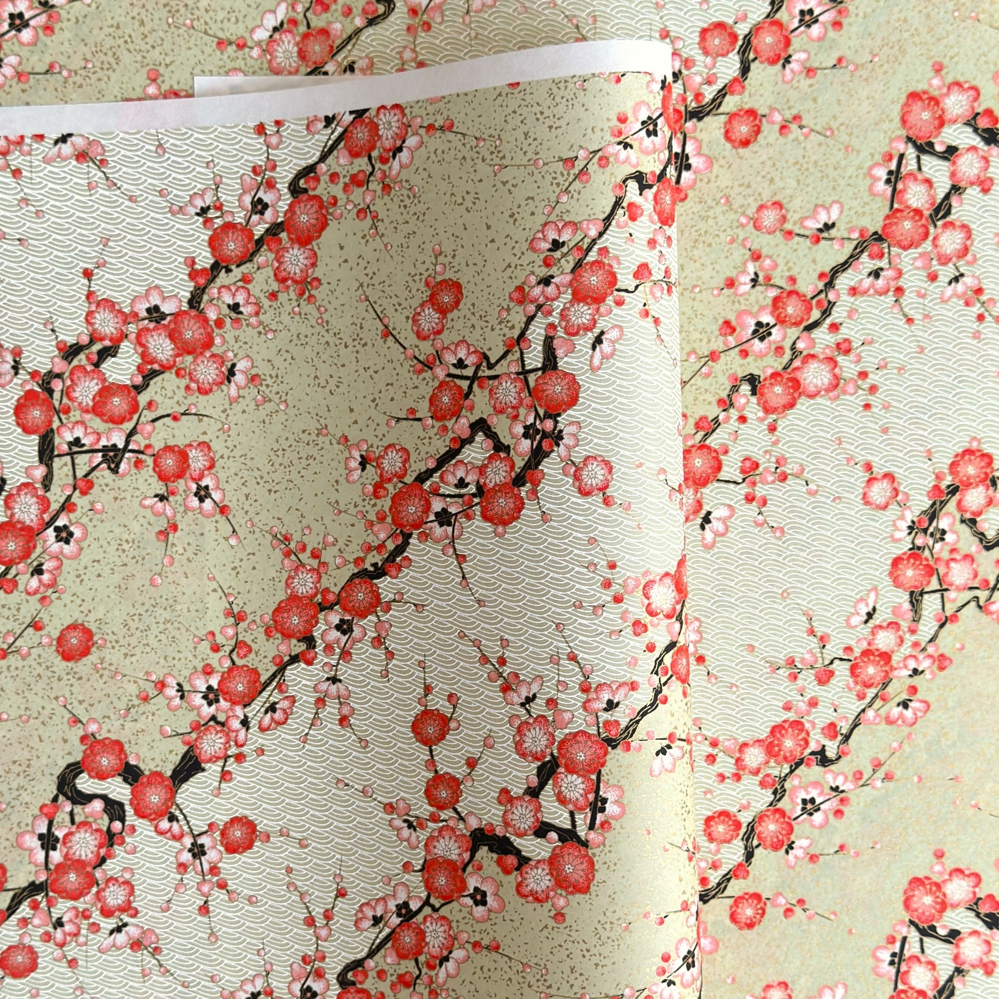 Japanese chiyogami silkscreen paper with diagonal branches of pink plum blossom on a sage green backdrop.