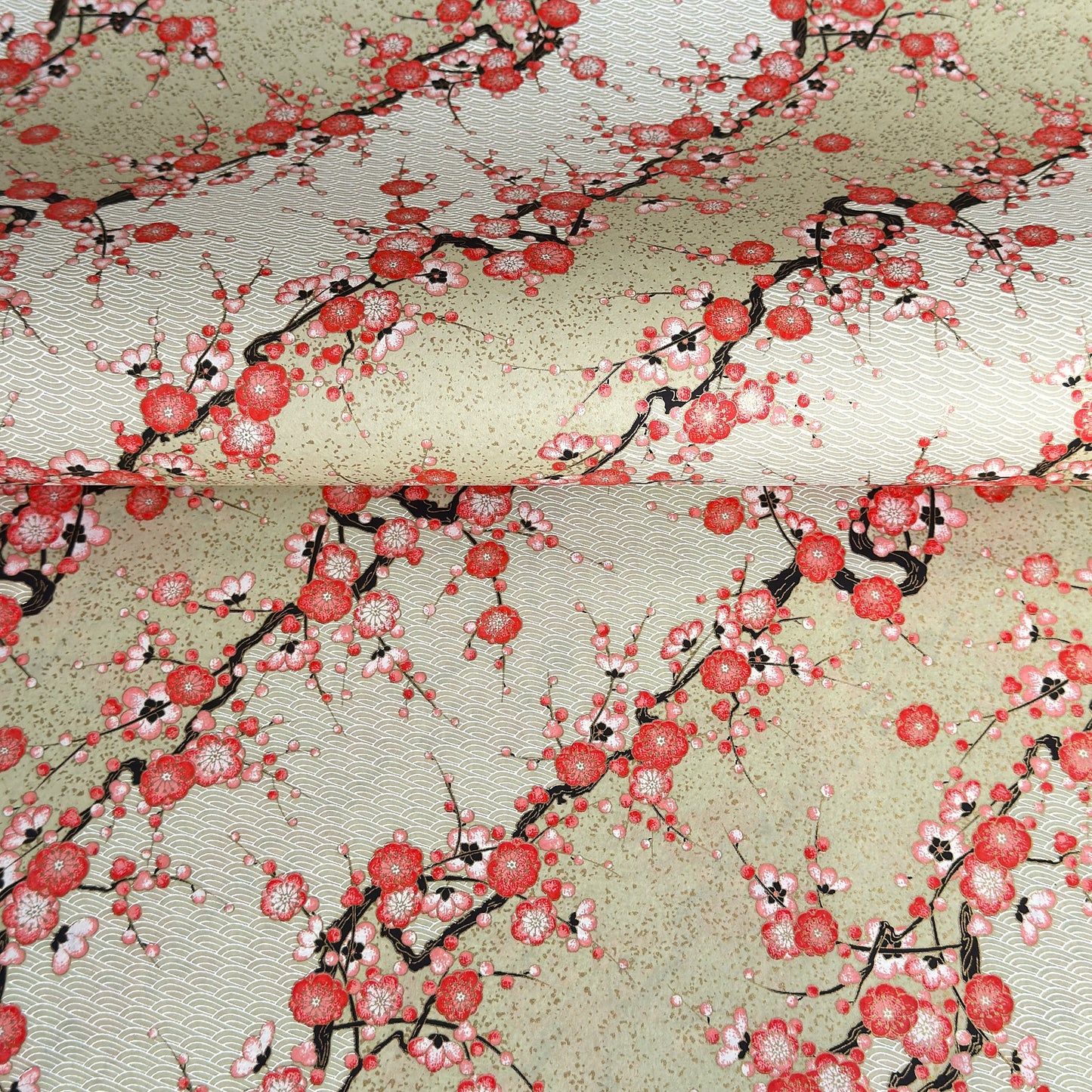 Japanese chiyogami silkscreen paper with diagonal branches of pink plum blossom on a sage green backdrop.