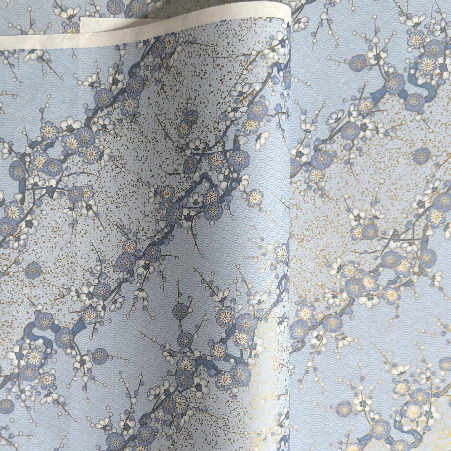 Japanese chiyogami paper with diagonal branches of sky blue plum blossom on a light blue background. 