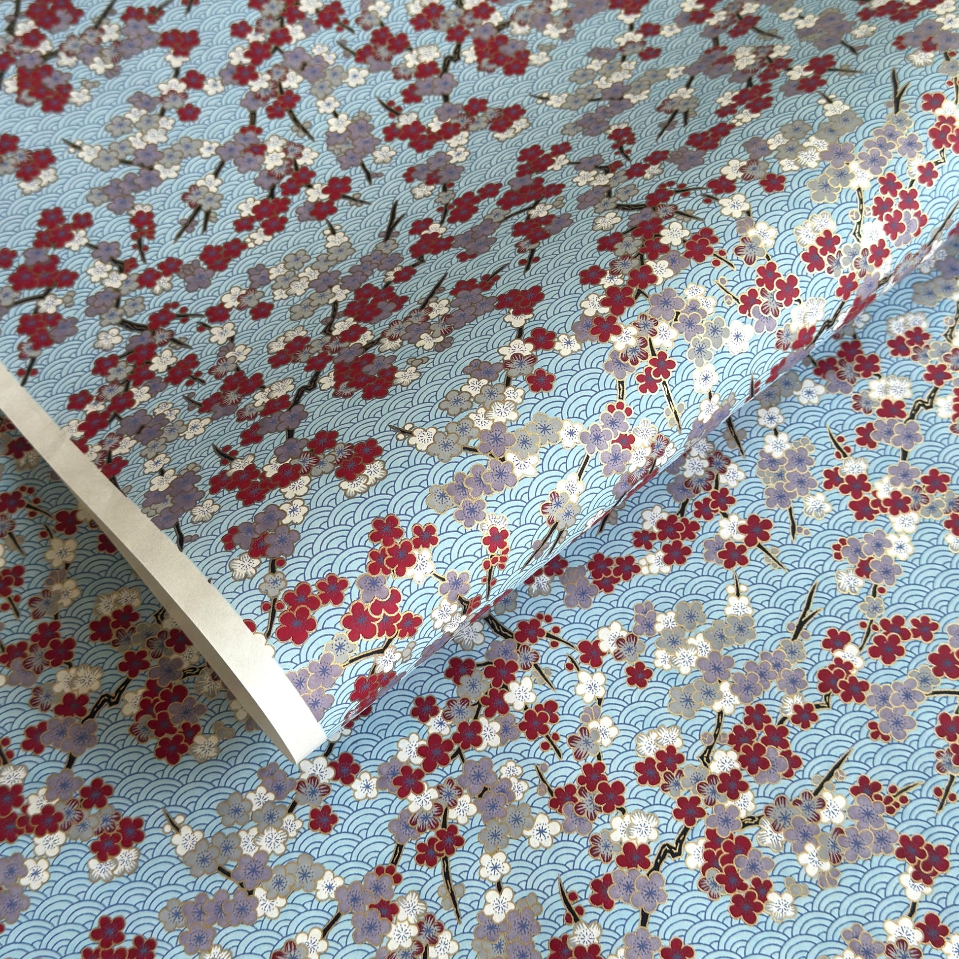 Japanese silkscreen chiyogami paper with a pattern of deep red, lilac and white plum blossom on a blue backdrop
