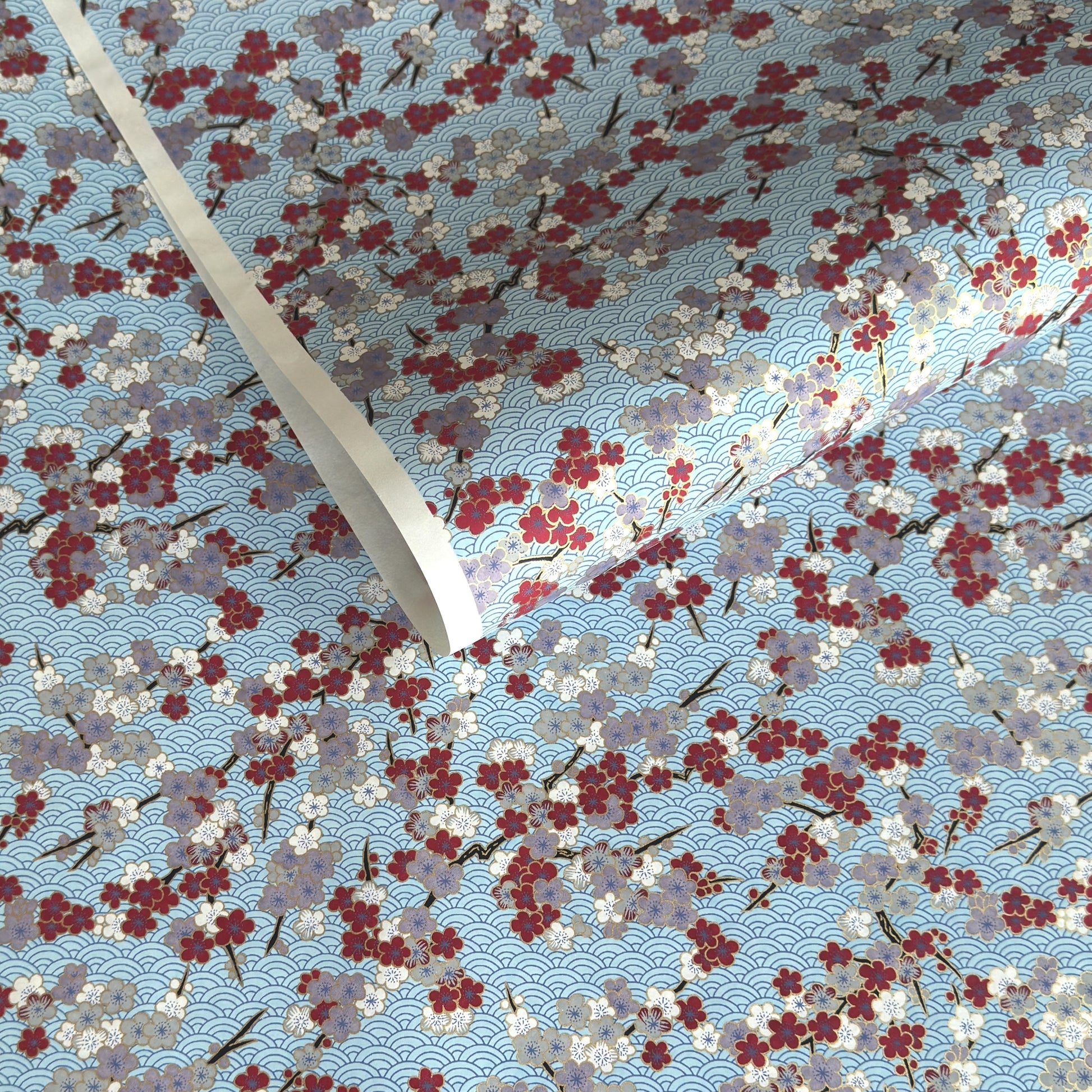 Japanese silkscreen chiyogami paper with a pattern of deep red, lilac and white plum blossom on a blue backdrop