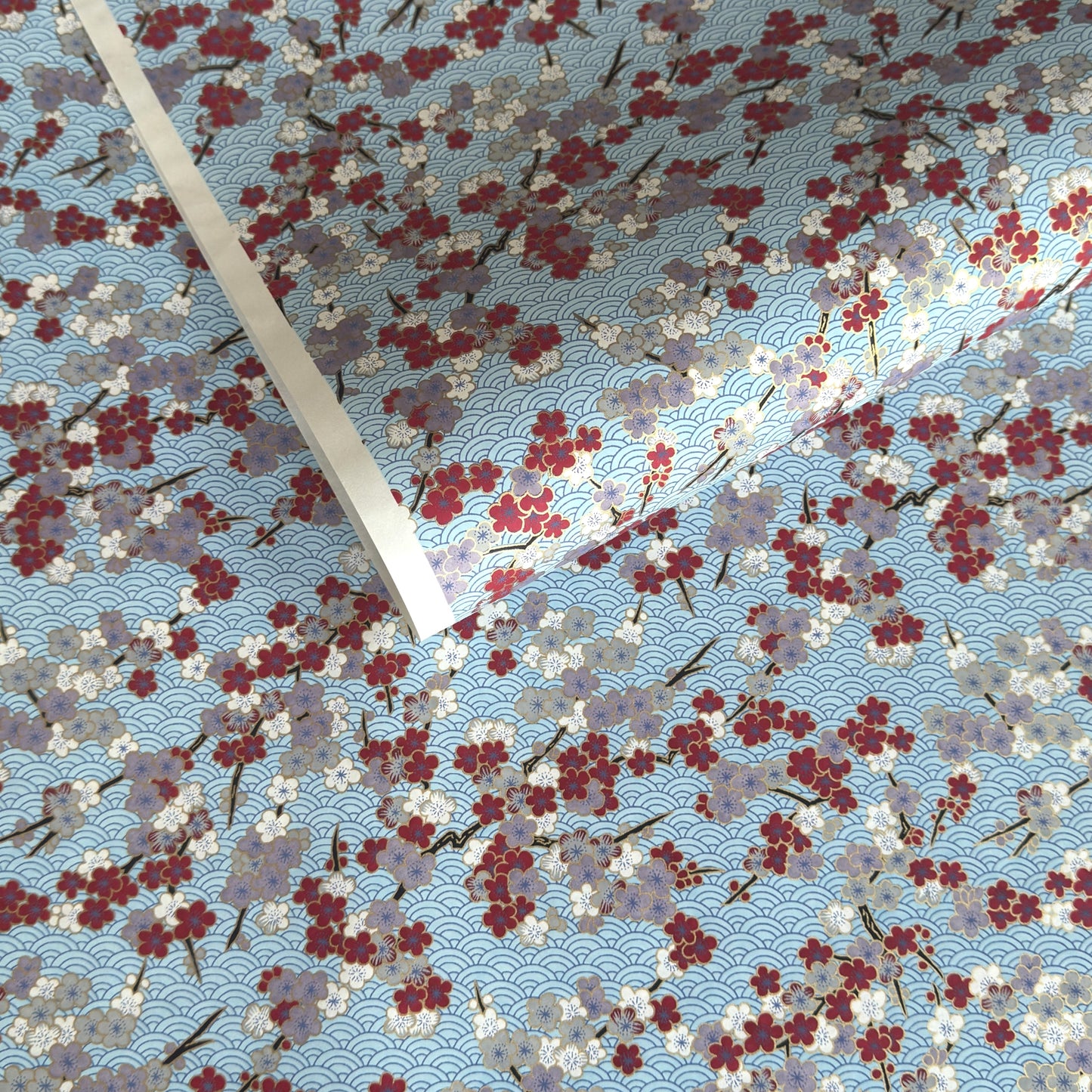 Japanese silkscreen chiyogami paper with a pattern of deep red, lilac and white plum blossom on a blue backdrop