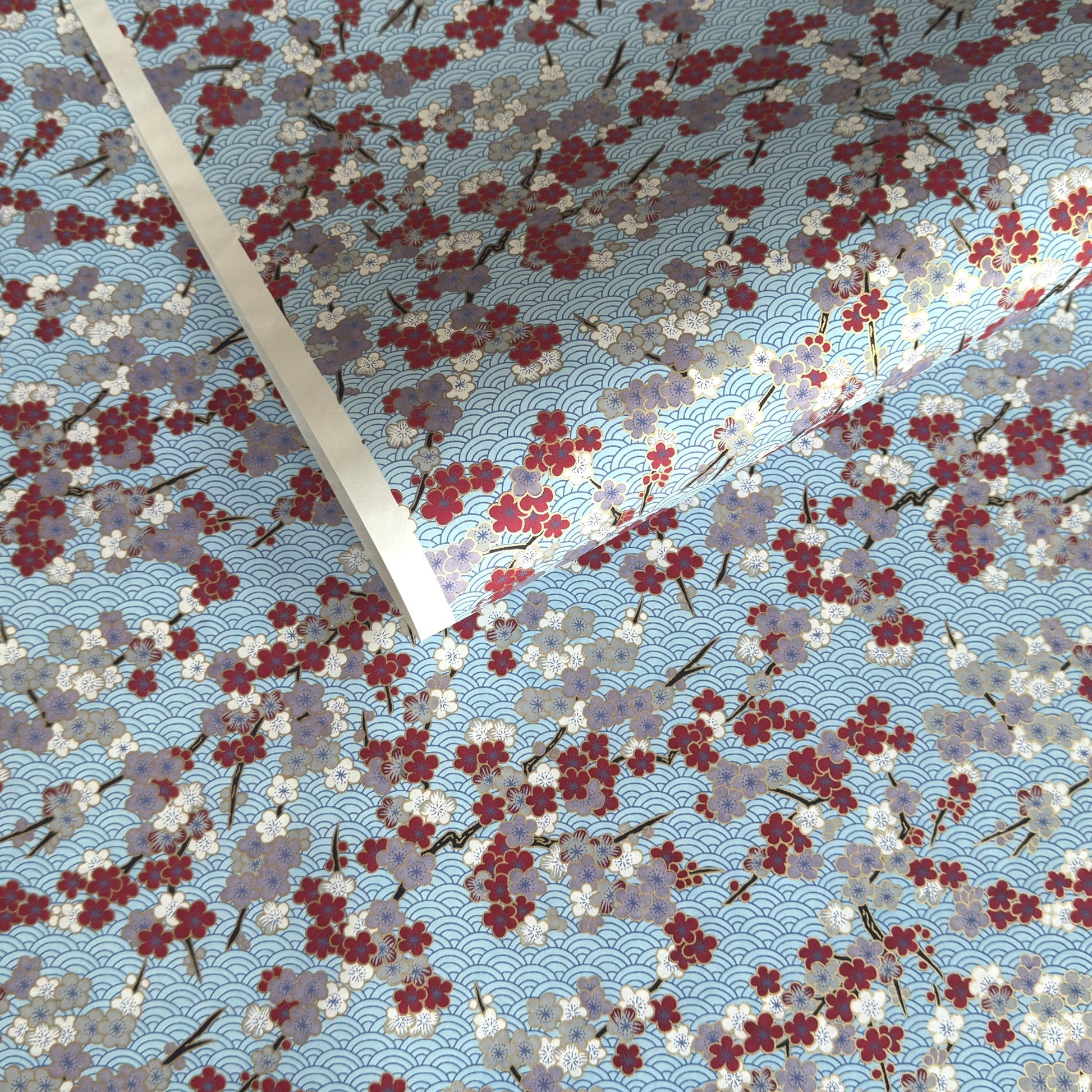 Japanese silkscreen chiyogami paper with a pattern of deep red, lilac and white plum blossom on a blue backdrop