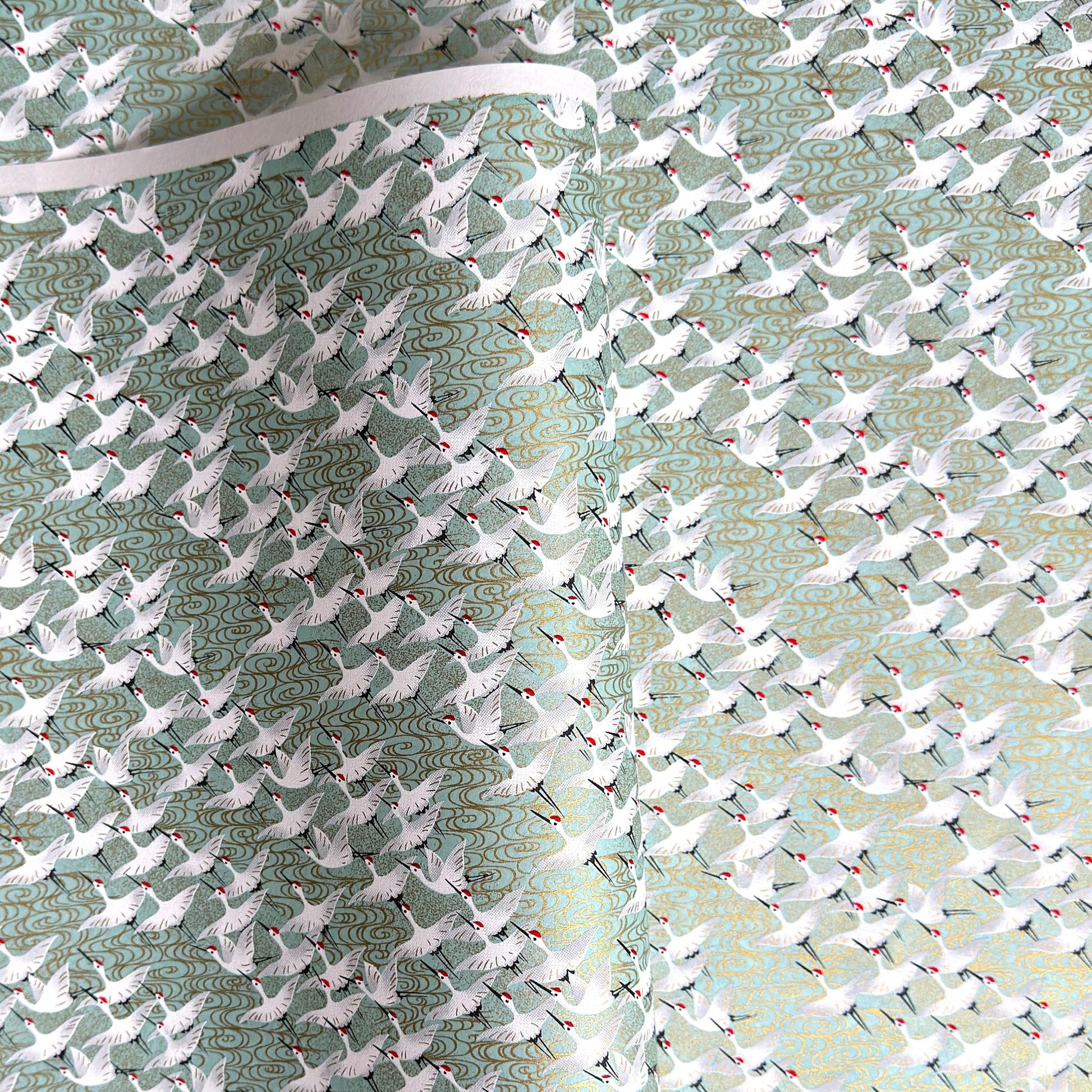 japanese silk-screen handmade paper showing white cranes in flight on a light teal and gold backdrop