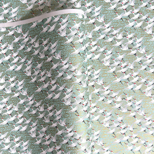 japanese silk-screen handmade paper showing white cranes in flight on a light teal and gold backdrop