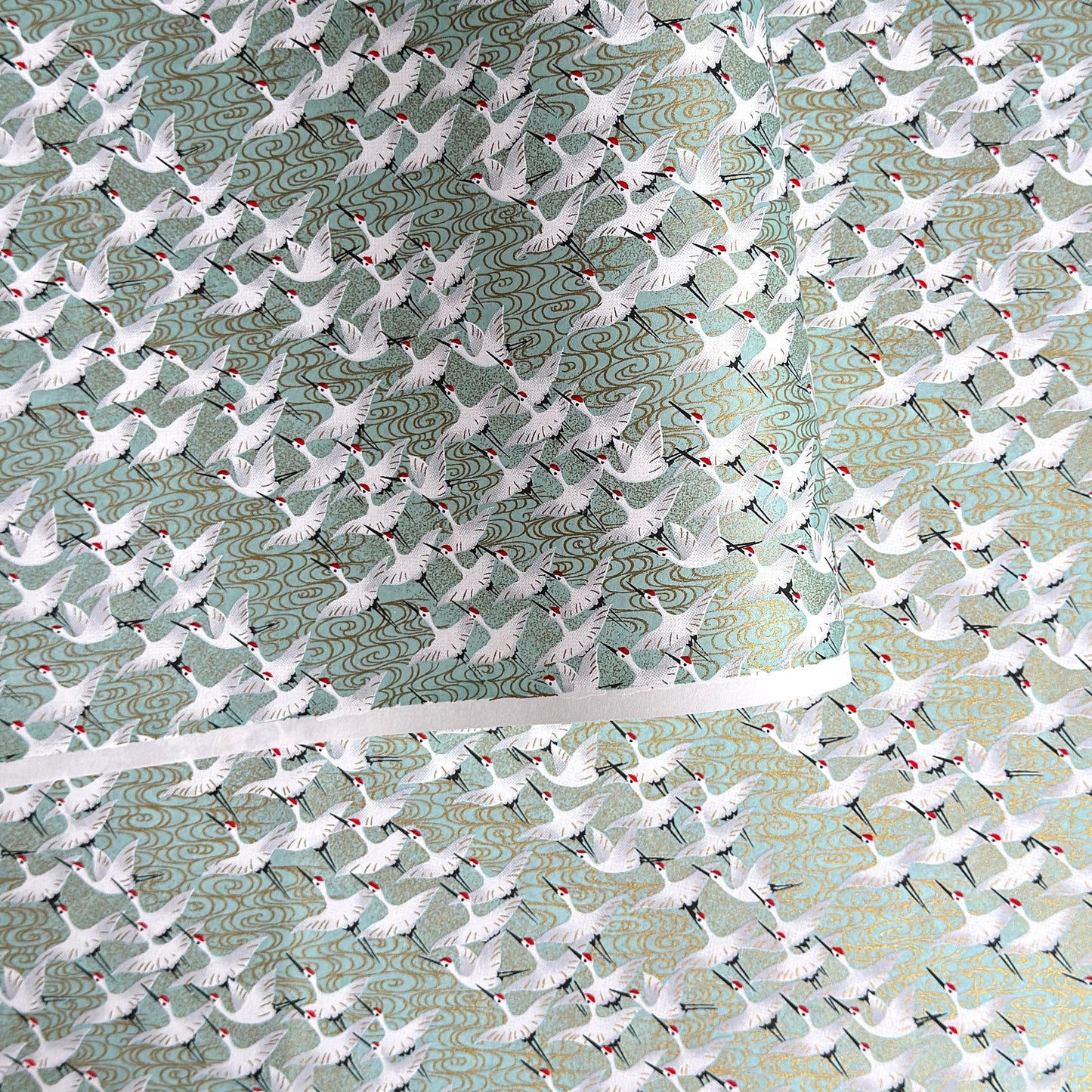 japanese silk-screen handmade paper showing white cranes in flight on a light teal and gold backdrop