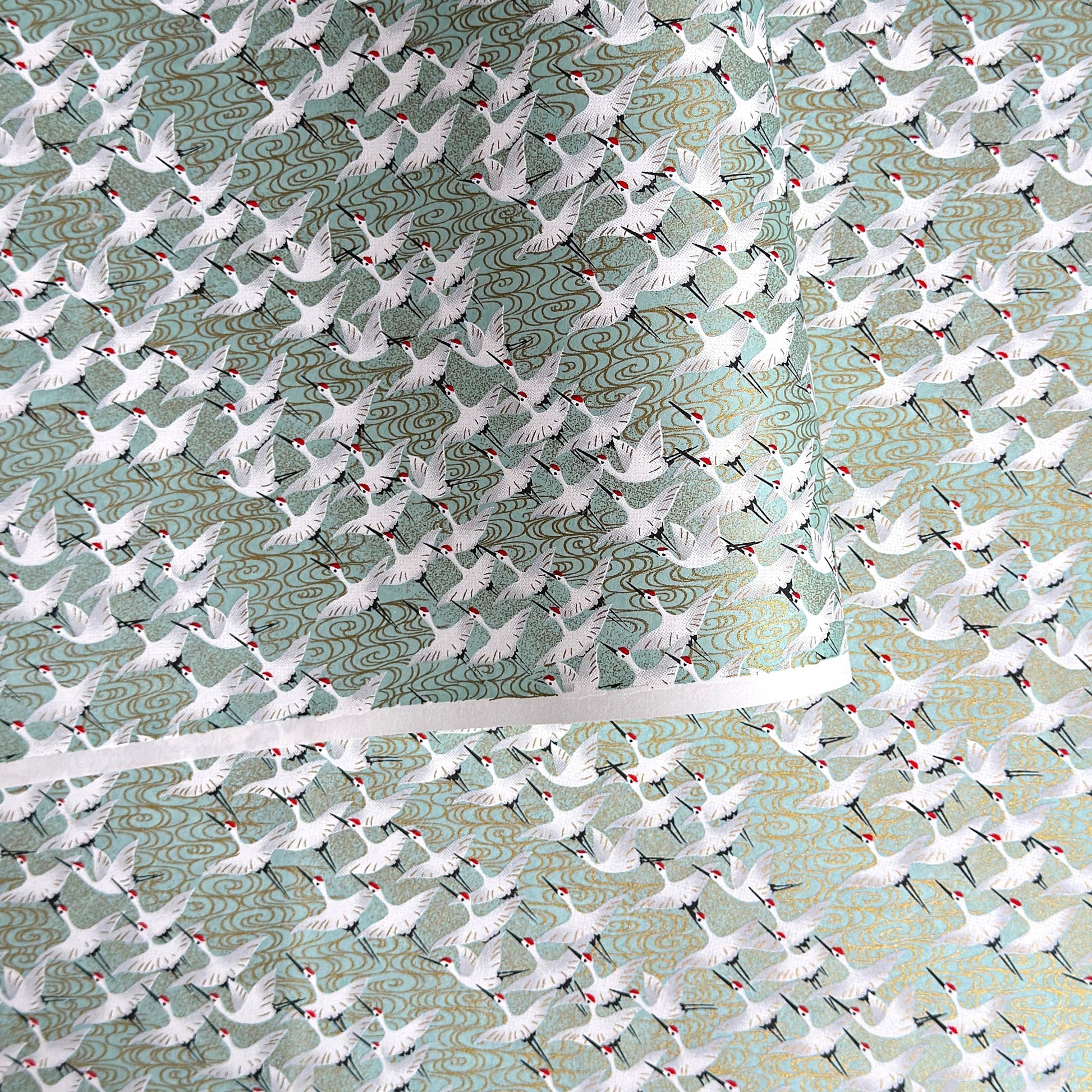 japanese silk-screen handmade paper showing white cranes in flight on a light teal and gold backdrop