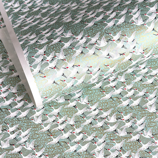 japanese silk-screen handmade paper showing white cranes in flight on a light teal and gold backdrop