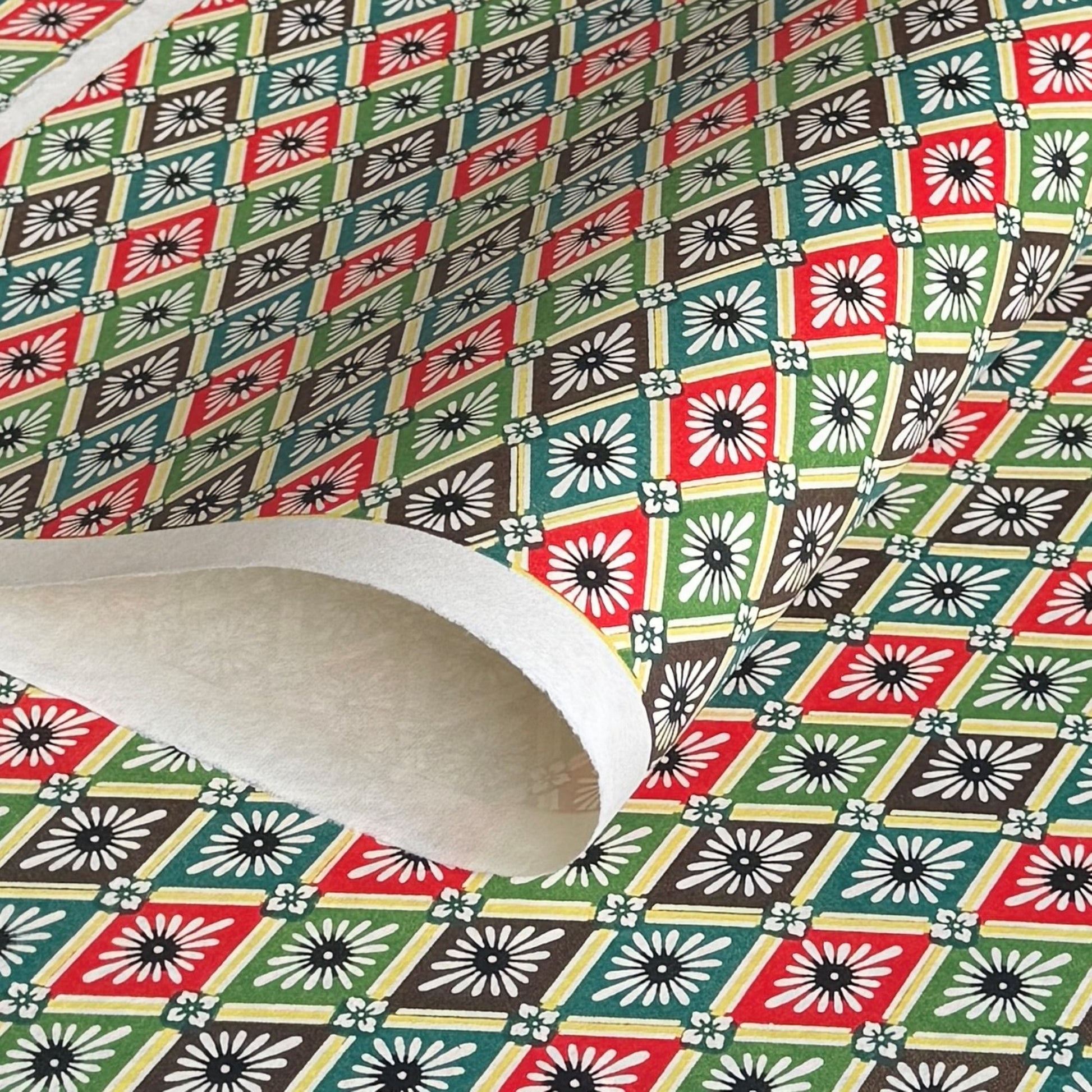 A sheet of katazome paper with a repeat rhombus pattern with the Japanese motif of the water caltrop plant (hishi) depicted alongside the four-petal flower of the water chestnut (hanabishi) in red, green. brown and teal.