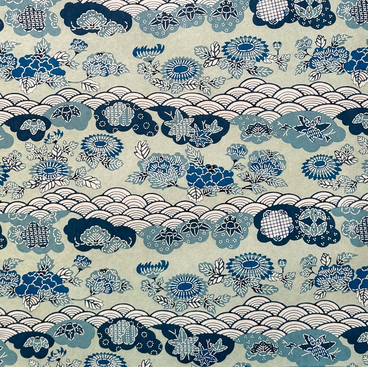 A colourful traditional pattern depicting stylised waves (seigaiha), flowers and foliage in a soft aqua and blue palette. A sheet of katazome paper