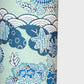 A colourful traditional pattern depicting stylised waves (seigaiha), flowers and foliage in a soft aqua and blue palette. A sheet of katazome paper. Close up