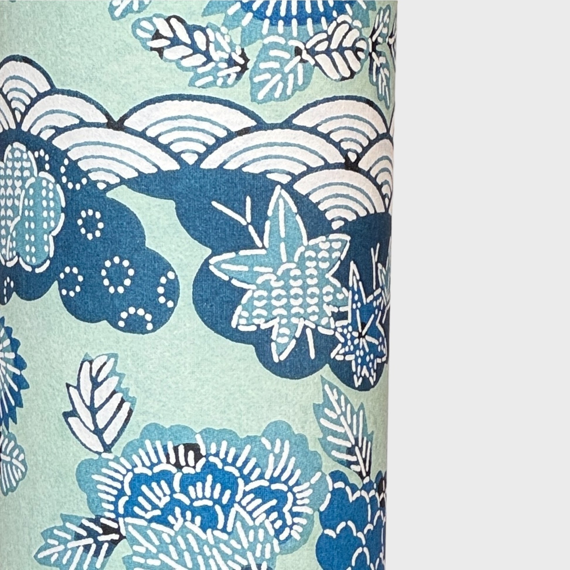A colourful traditional pattern depicting stylised waves (seigaiha), flowers and foliage in a soft aqua and blue palette. A sheet of katazome paper. Close up