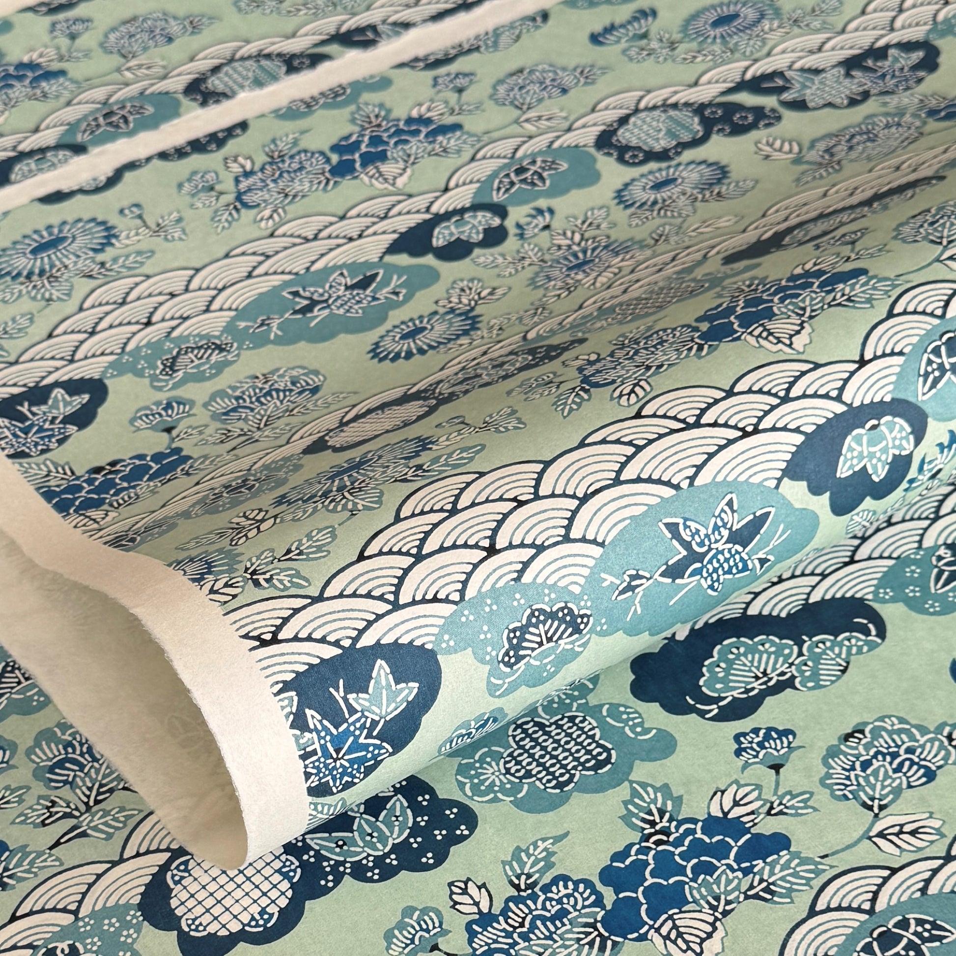 A colourful traditional pattern depicting stylised waves (seigaiha), flowers and foliage in a soft aqua and blue palette. A sheet of katazome paper