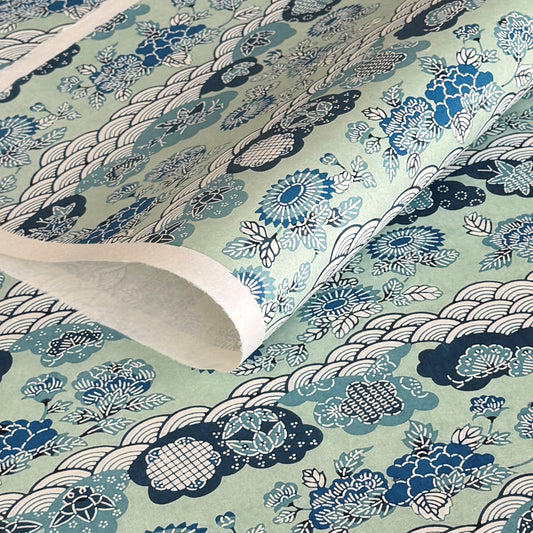 A colourful traditional pattern depicting stylised waves (seigaiha), flowers and foliage in a soft aqua and blue palette. A sheet of katazome paper. Close up