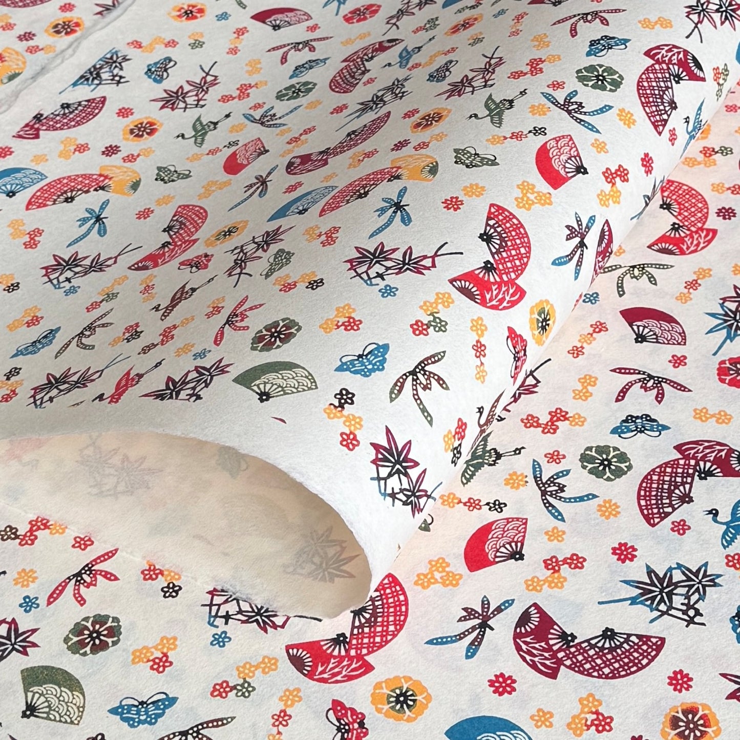 Folding fans (sensu) and cranes (tsuru) amongst flowers and foliage.  A multicoloured pattern on Japanese katazome paper