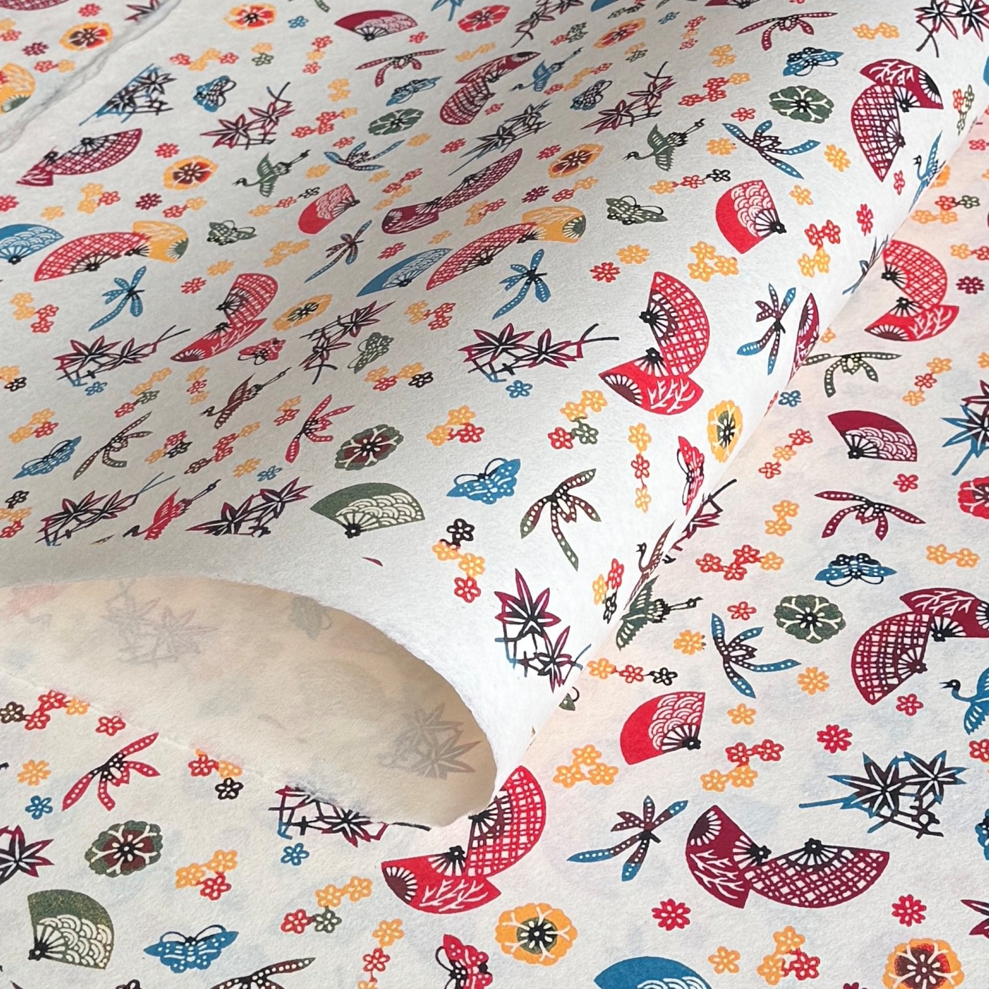 Folding fans (sensu) and cranes (tsuru) amongst flowers and foliage.  A multicoloured pattern on Japanese katazome paper