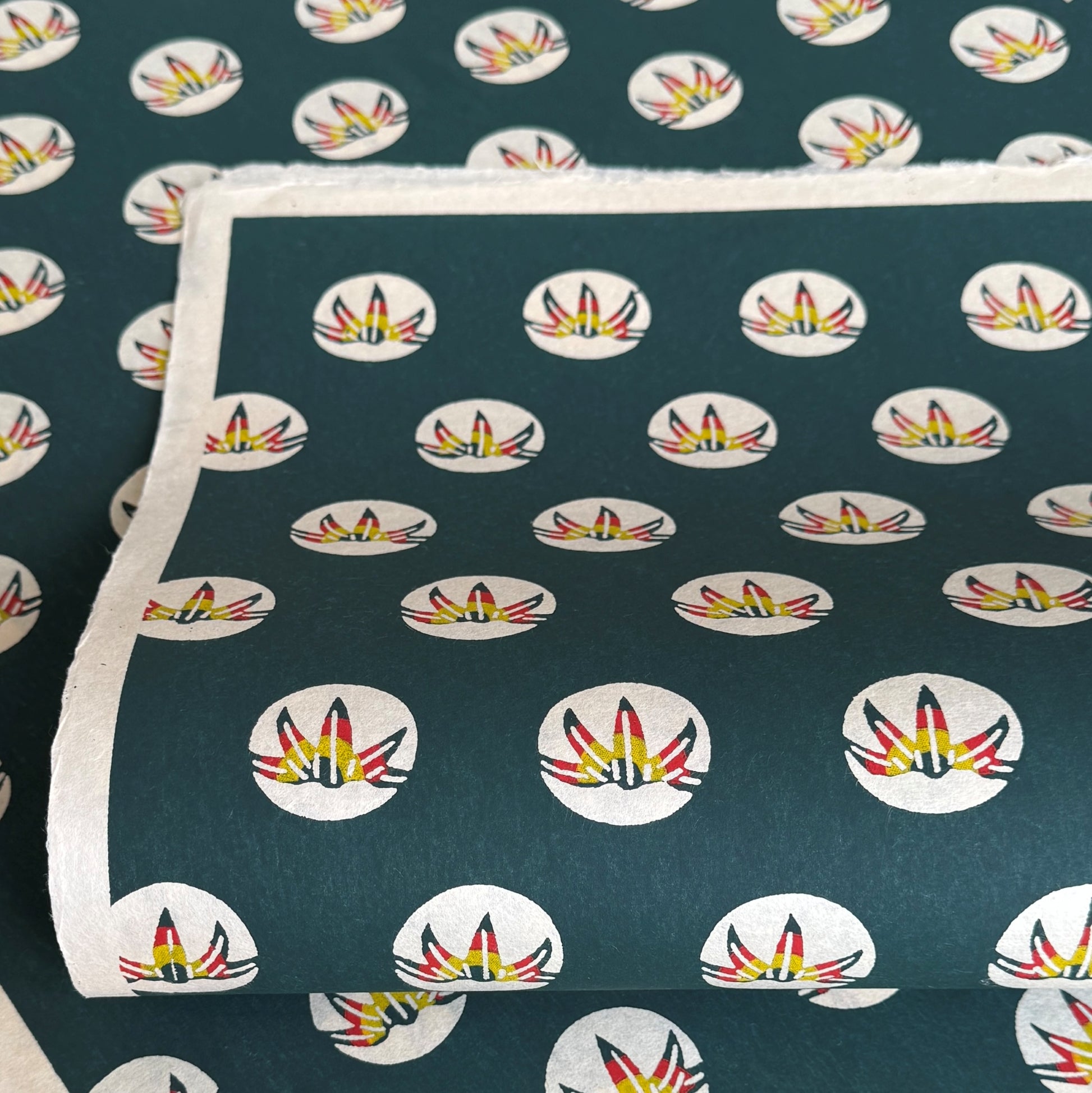 Traditional pattern a Japanese circular crest of a colourful lotus flower on a dark teal.  A sheet of katazome paper