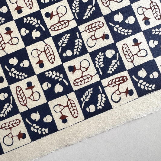 Japanese katazome-shi paper in navy blue and cream chequerboard pattern with motifs of autumn - acorns and wheat. Close up