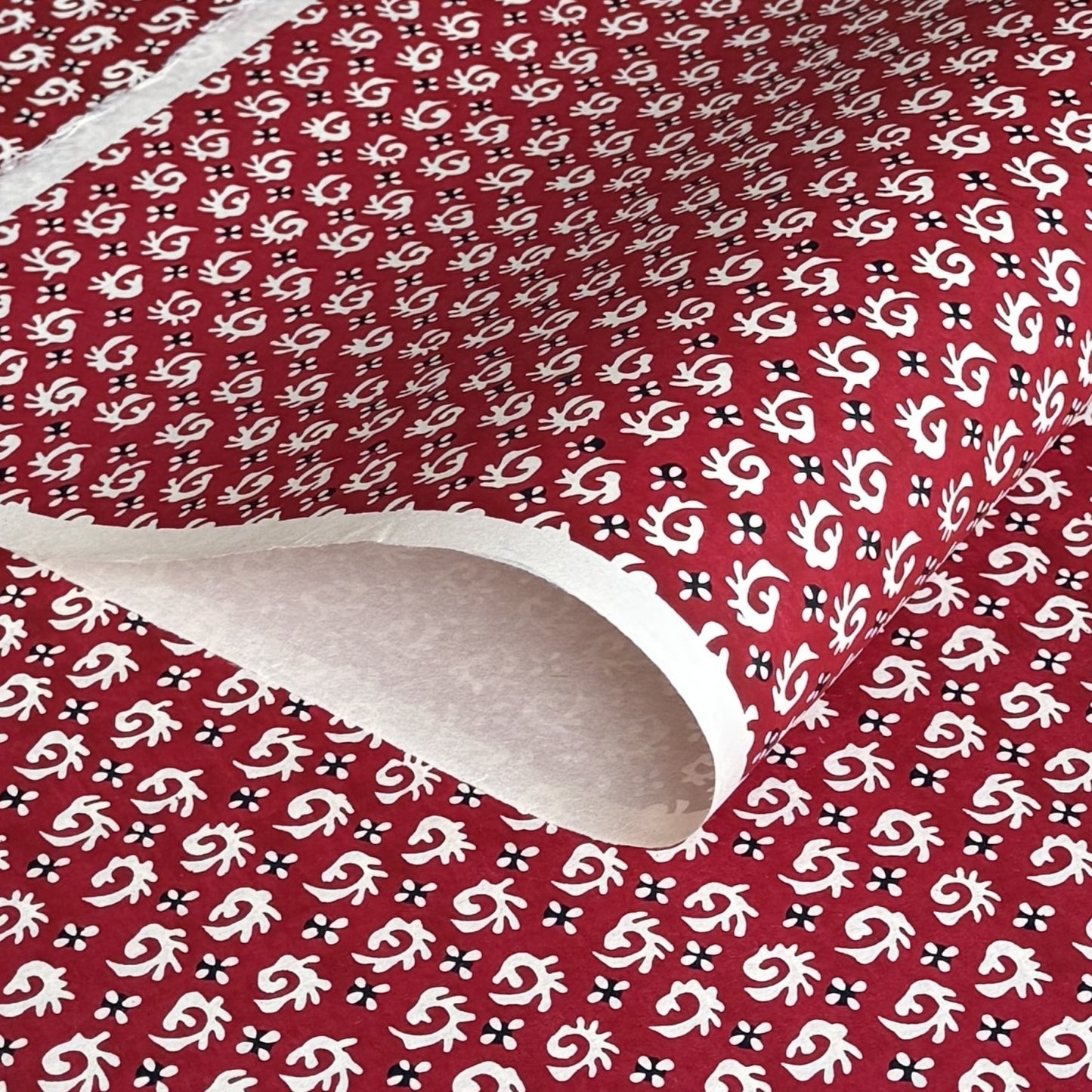 A Japanese stencil-dyed patterned paper with a repeat pattern in white on a deep rich red background.