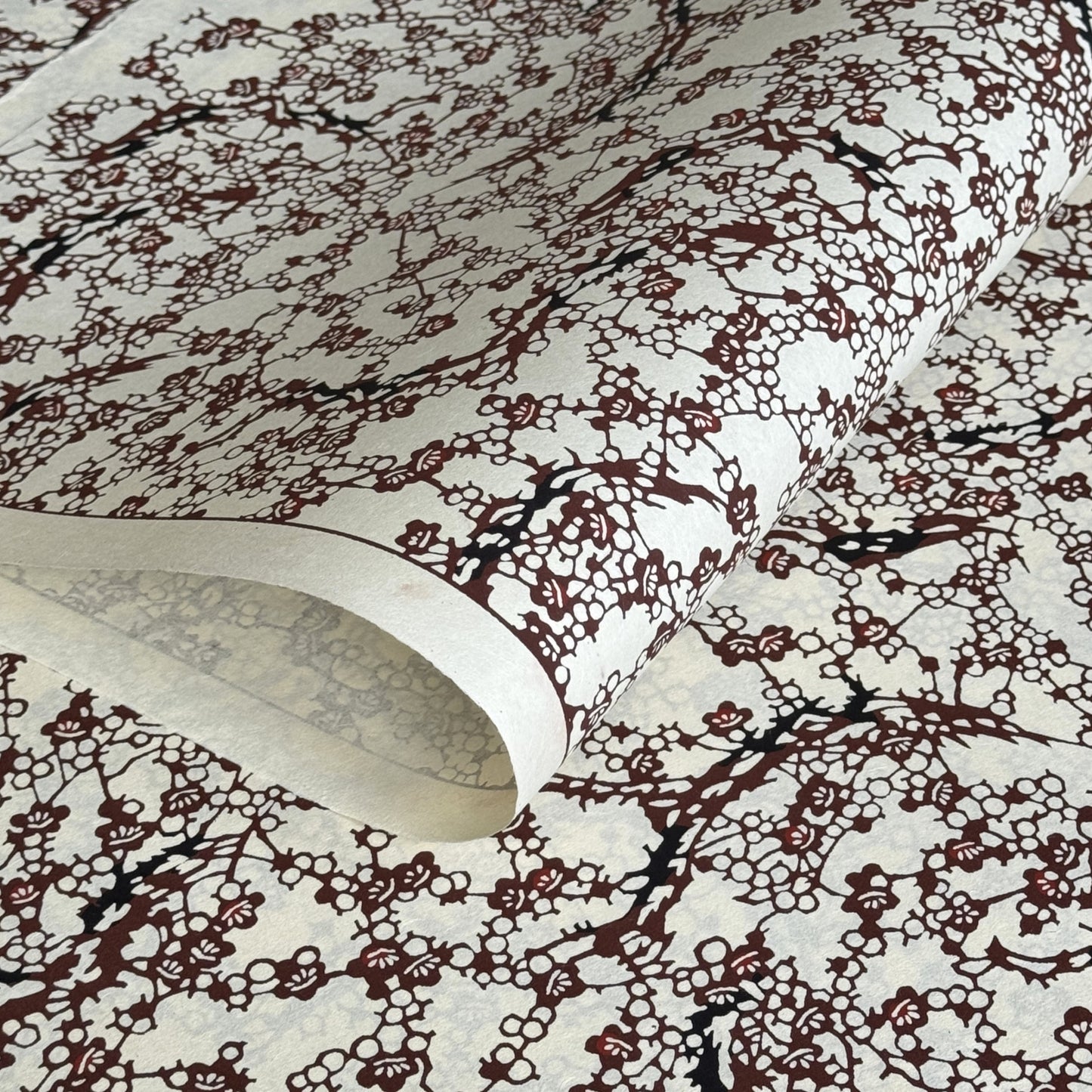 Japanese kazazome-shi stenciled dyed paper with a pattern of branches of plum blossom in deep maroon and black on an ivory paper.