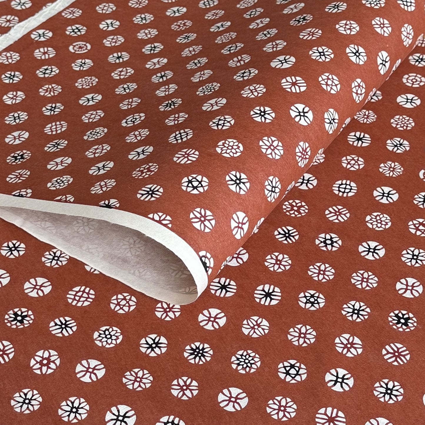A Japanese stencil-dyed patterned paper with a repeat pattern of floral motif circles on a rich tan brown base
