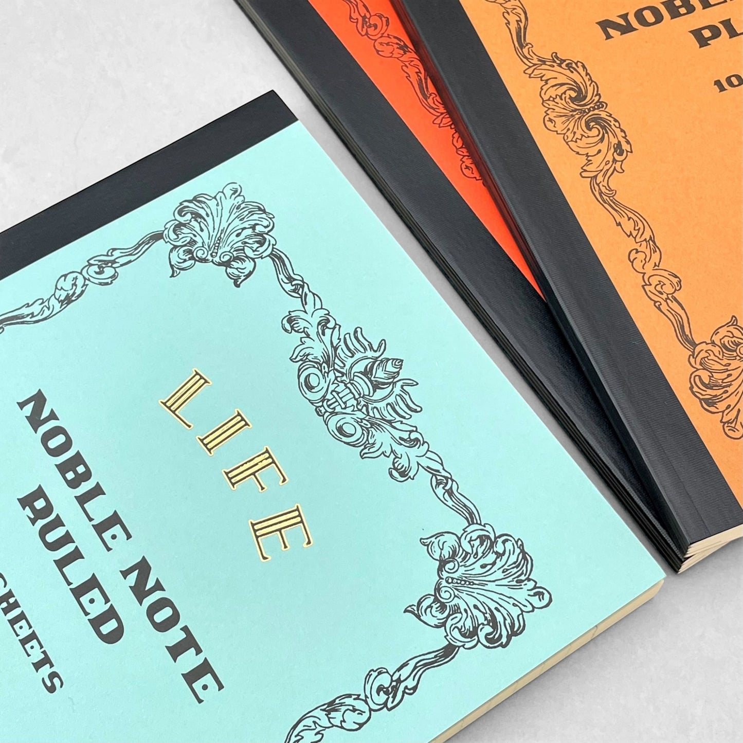 Softcover notebook with lined pages. The cover is plain aqua with a decorative black border and branding, Life Noble Ruled by Japanese brand Life