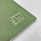 A5 soft cover notebook, cover is olive green with a small white grid pattern by Japanese brand Kleid