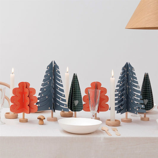 A blue paper fir tree decoration by Jurianne Matter, pictured on a table with other paper trees