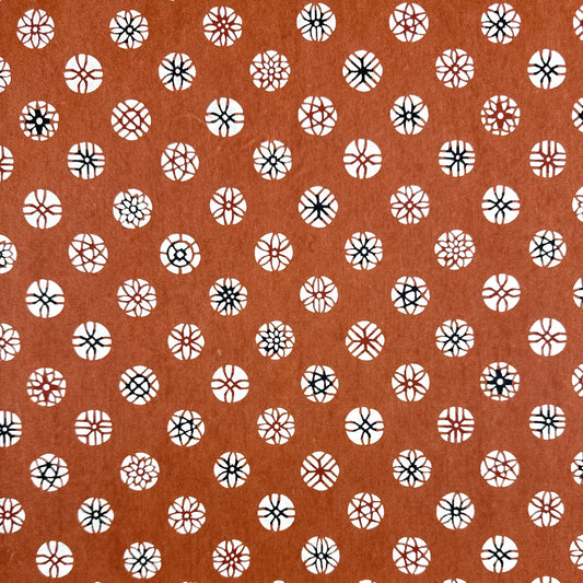 A Japanese stencil-dyed patterned paper with a repeat pattern of floral motif circles on a rich tan brown base