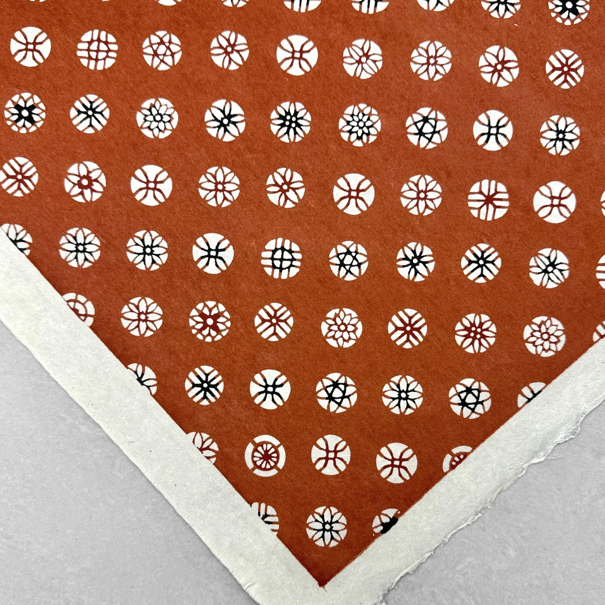 A Japanese stencil-dyed patterned paper with a repeat pattern of floral motif circles on a rich tan brown base. Close up