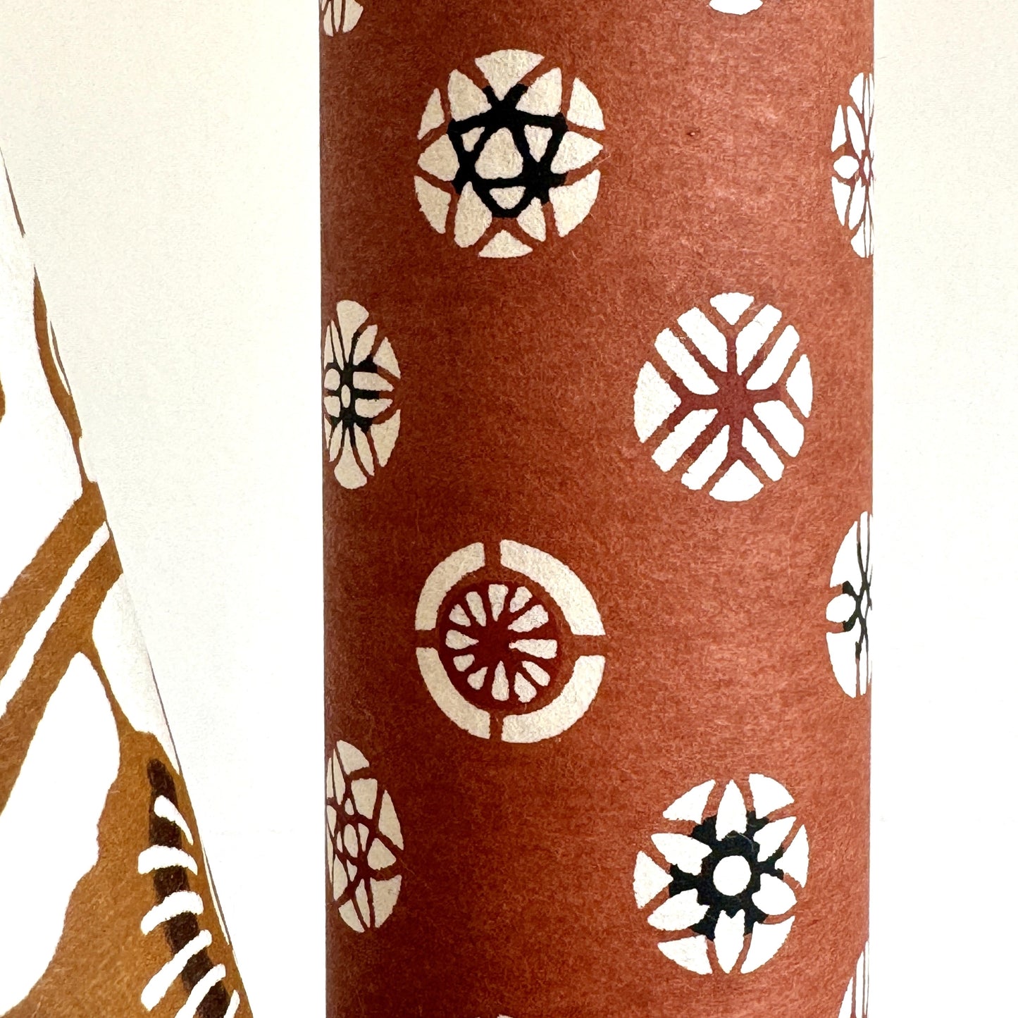 A Japanese stencil-dyed patterned paper with a repeat pattern of floral motif circles on a rich tan brown base. Close-up