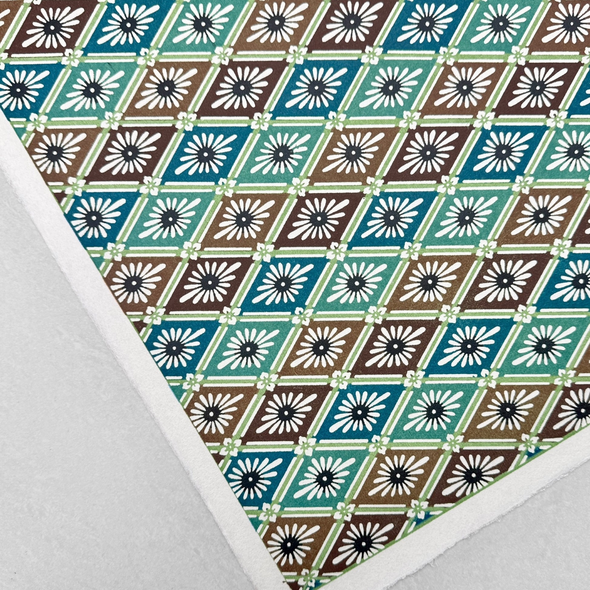 A Japanese stencil-dyed patterned paper with a repeat pattern of floral diamonds in tones of blue, aqua, brown and white. Close-up, flat view