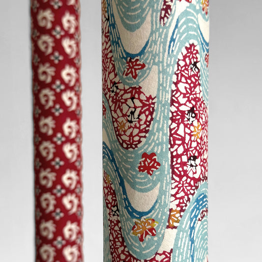 Japanese stencil-dyed paper with a pattern of a stylised blue river and dark red banks of flowers. Close up