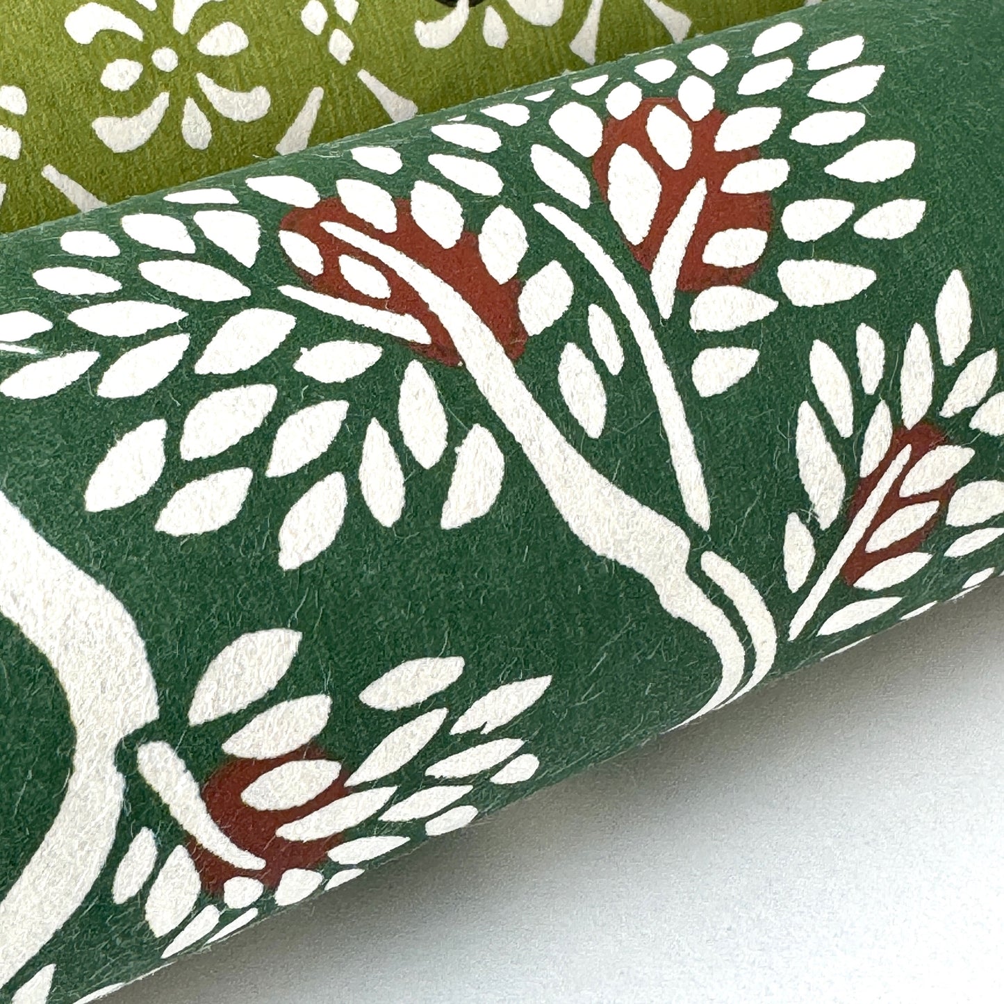 A Japanese stencil-dyed patterned paper in dark green with a repeat pattern of white bonsai trees. Close-up, rolled 