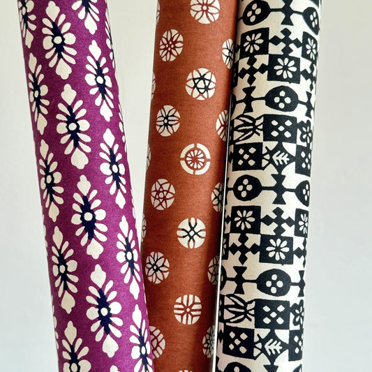 japanese katazome-shi paper (stencil-dyed) with a white and black repeat pattern on purple. Pictured rolled with other patterned designs.