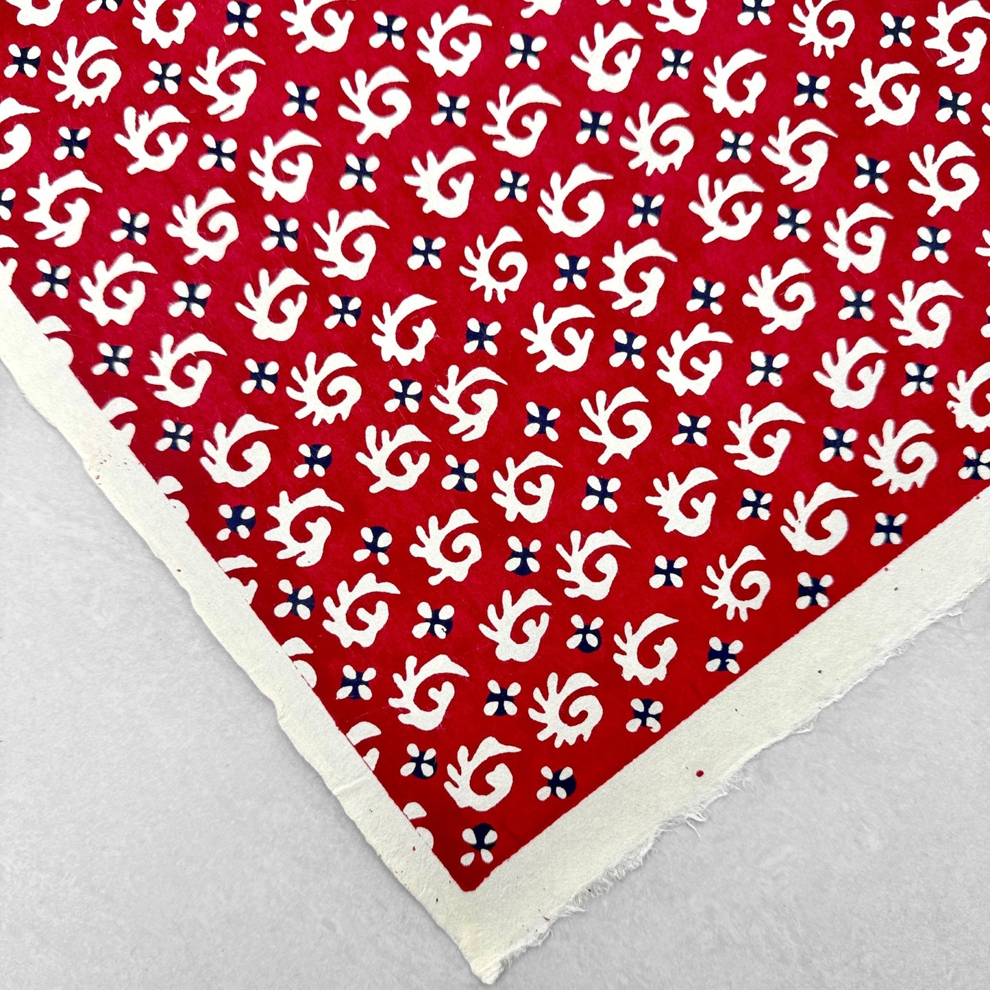 A Japanese stencil-dyed patterned paper with a repeat pattern in white on a deep rich red background. Flat view